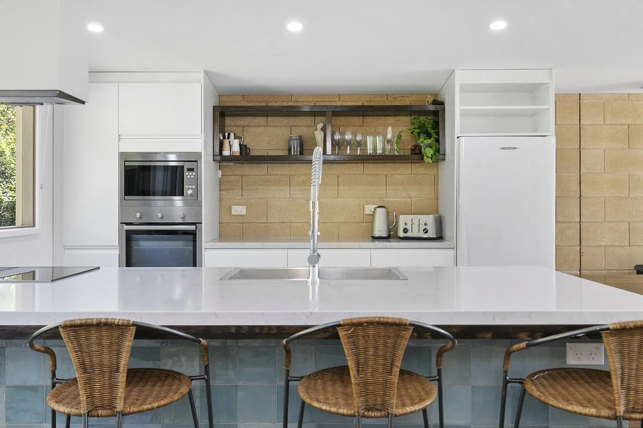 A bright kitchen with a wide island and woven seating.