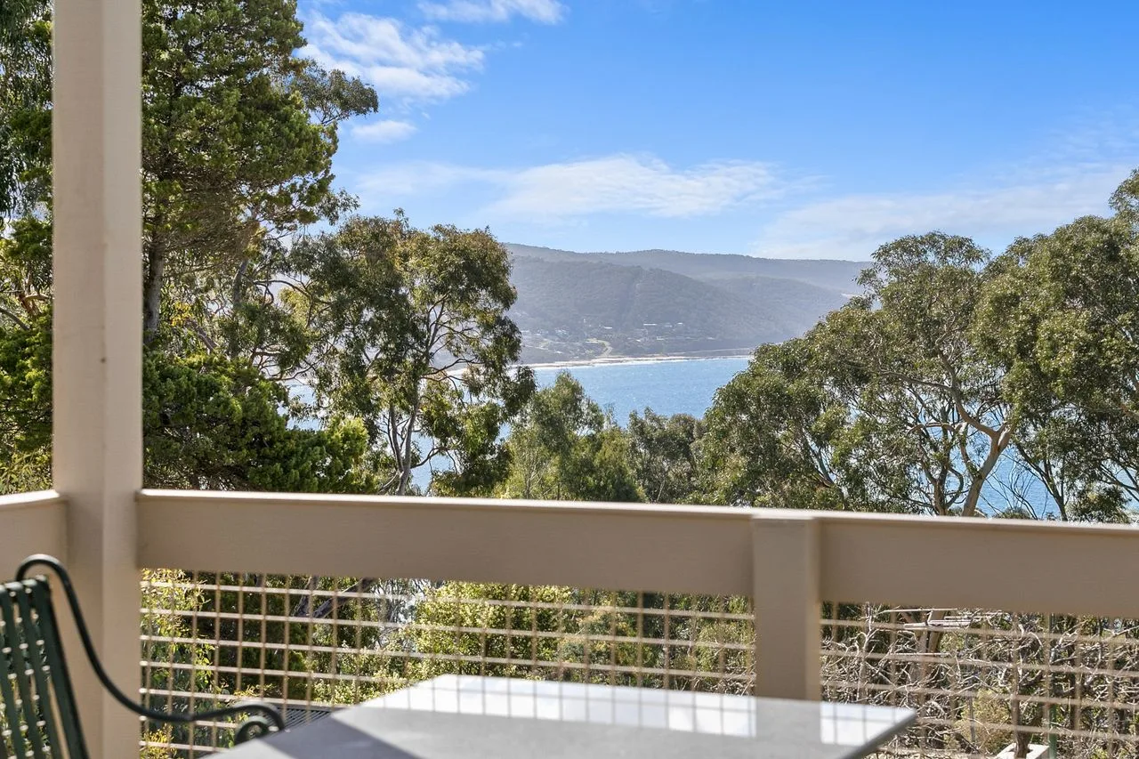 A balcony overlooks trees, a bay, and distant hills.