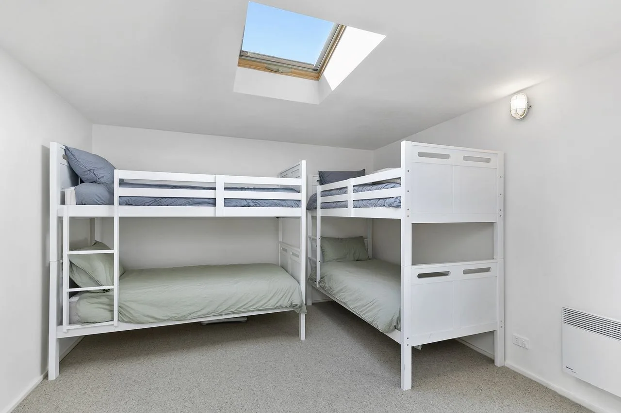 A bedroom with white bunk beds beneath a skylight.