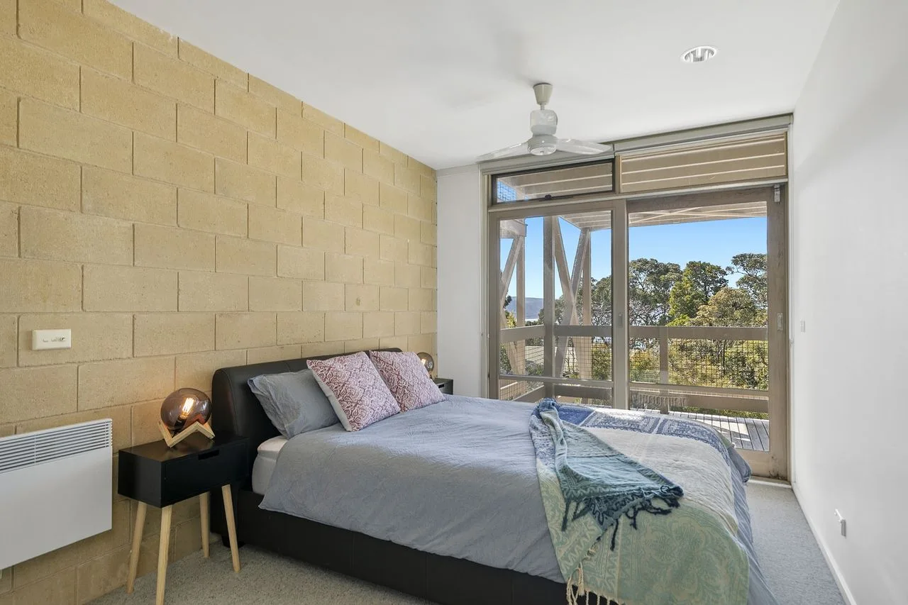 A bedroom with a bed beside large windows opening onto a balcony.