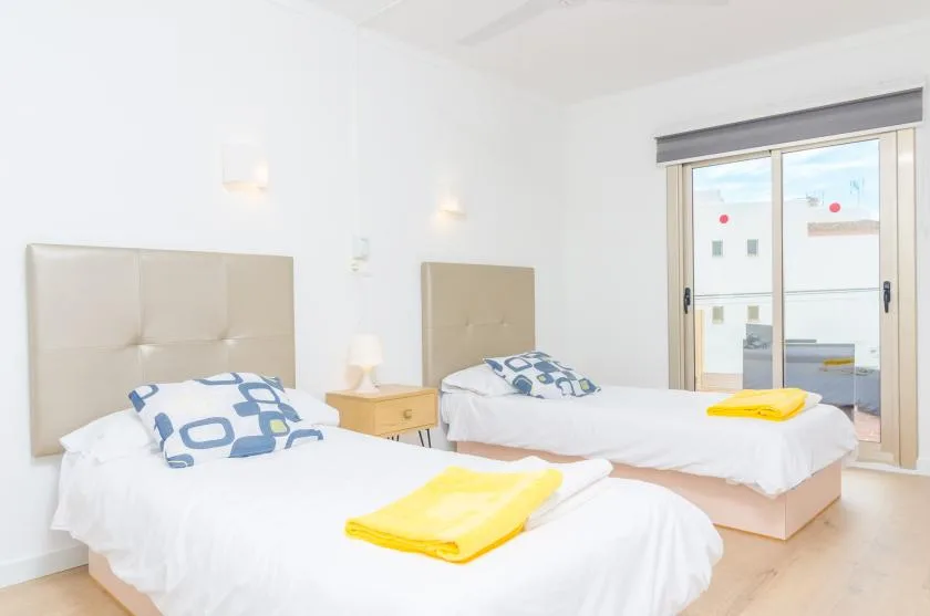 A bright bedroom with two single beds, white bedding, and yellow towels.