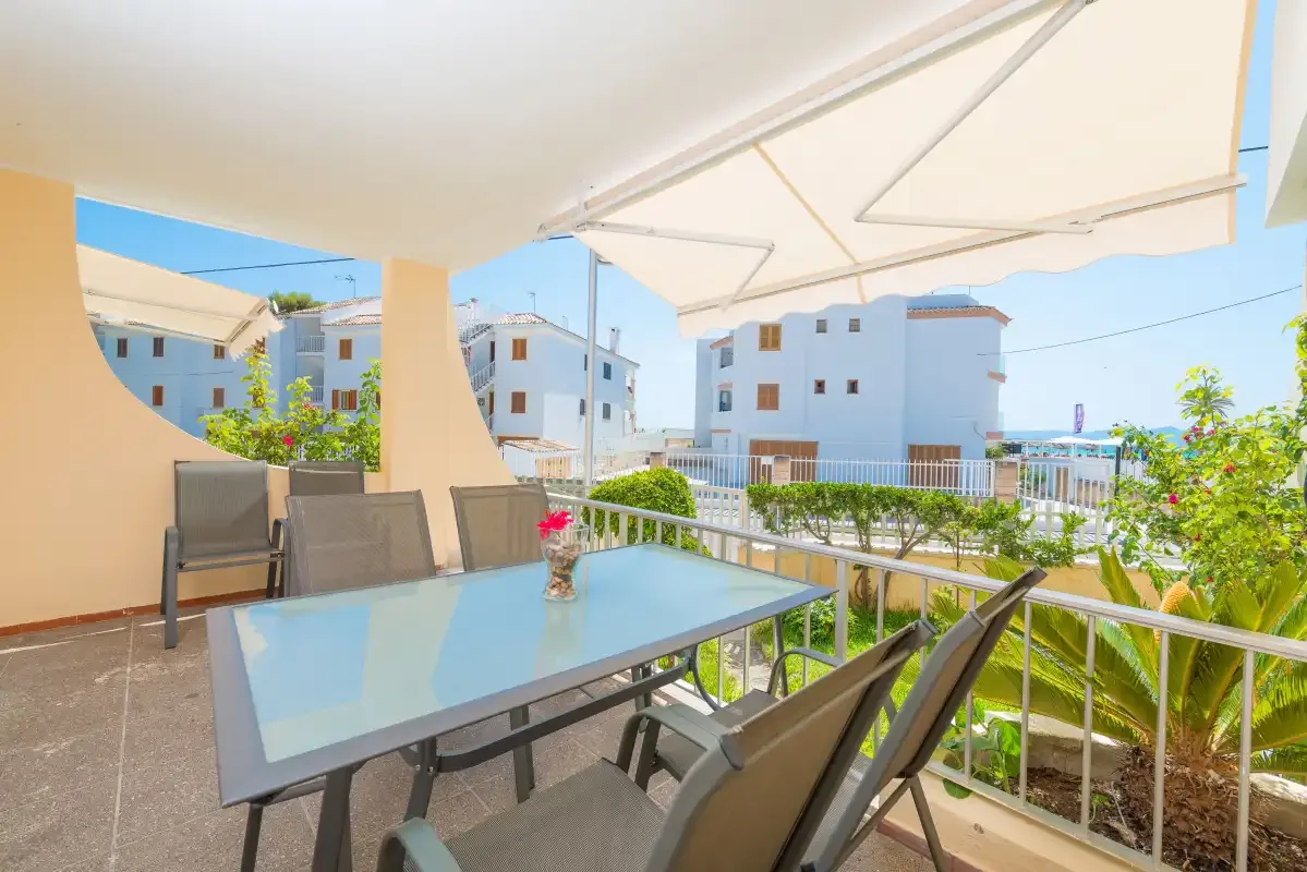 A shaded outdoor dining area has a glass table and views of nearby buildings.