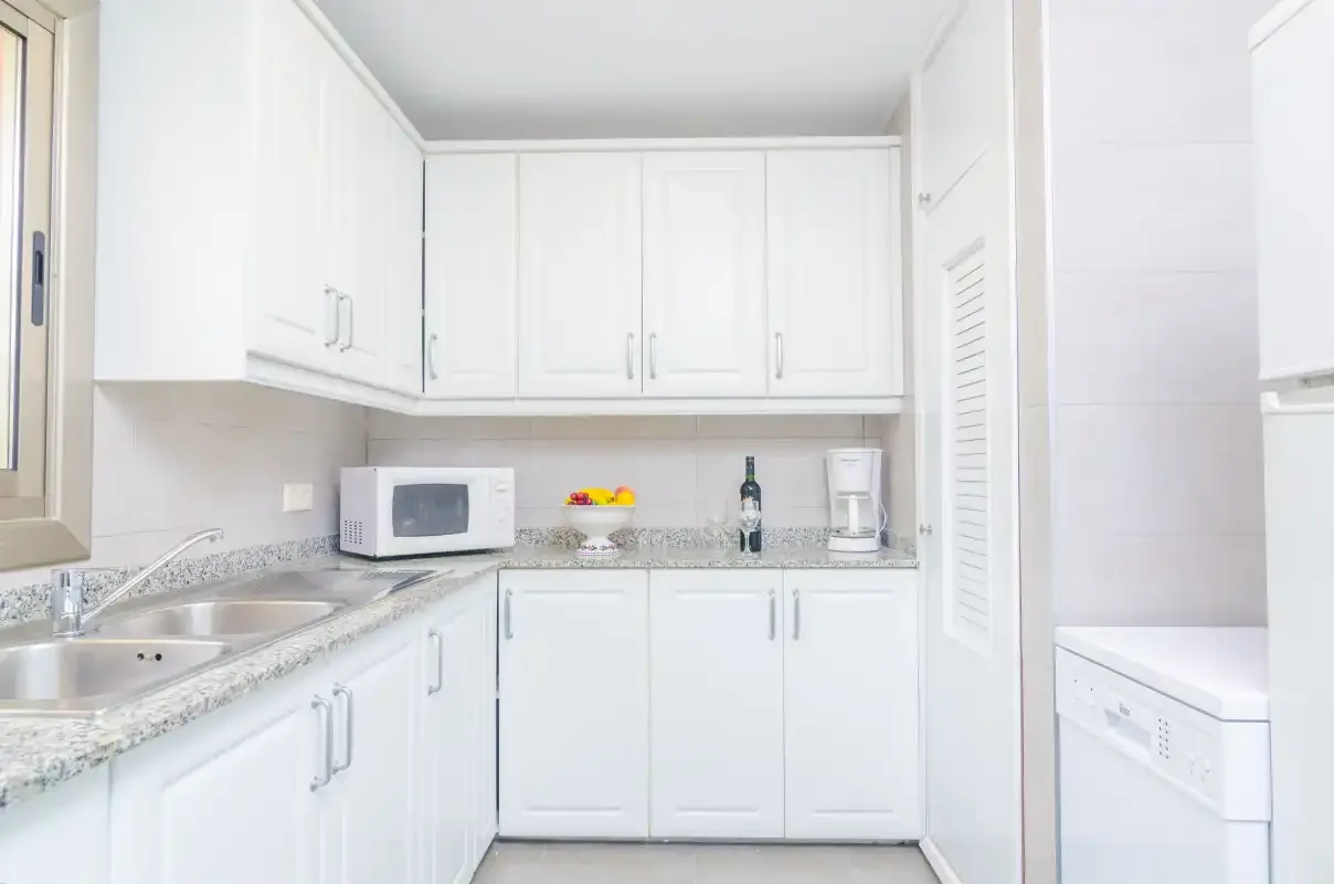 A bright white kitchen with a countertop microwave and sink.