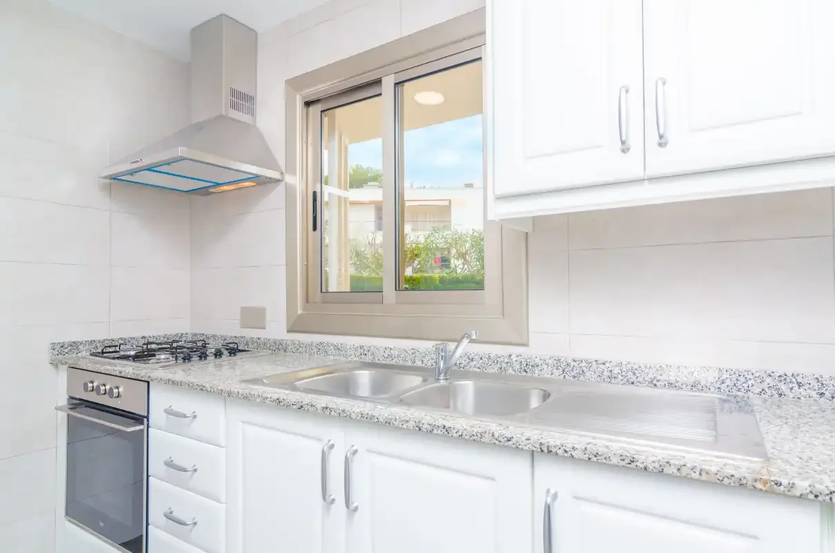 A bright kitchen with a countertop, sink, stove, and window.