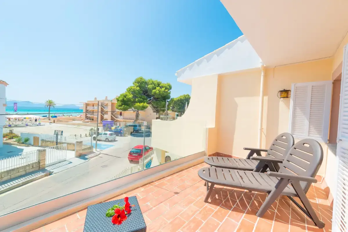 A sunny balcony has two reclining chairs overlooking the beach and nearby buildings.