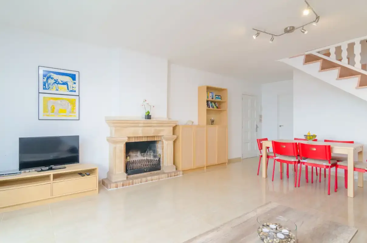 A bright living and dining area with a fireplace, television, and red dining chairs.
