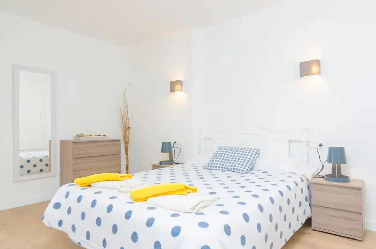 A bright bedroom has a bed with blue-patterned bedding and bedside lamps.