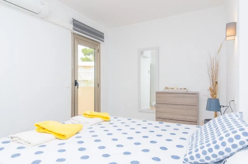 A bright bedroom with a bed covered in white and blue bedding.