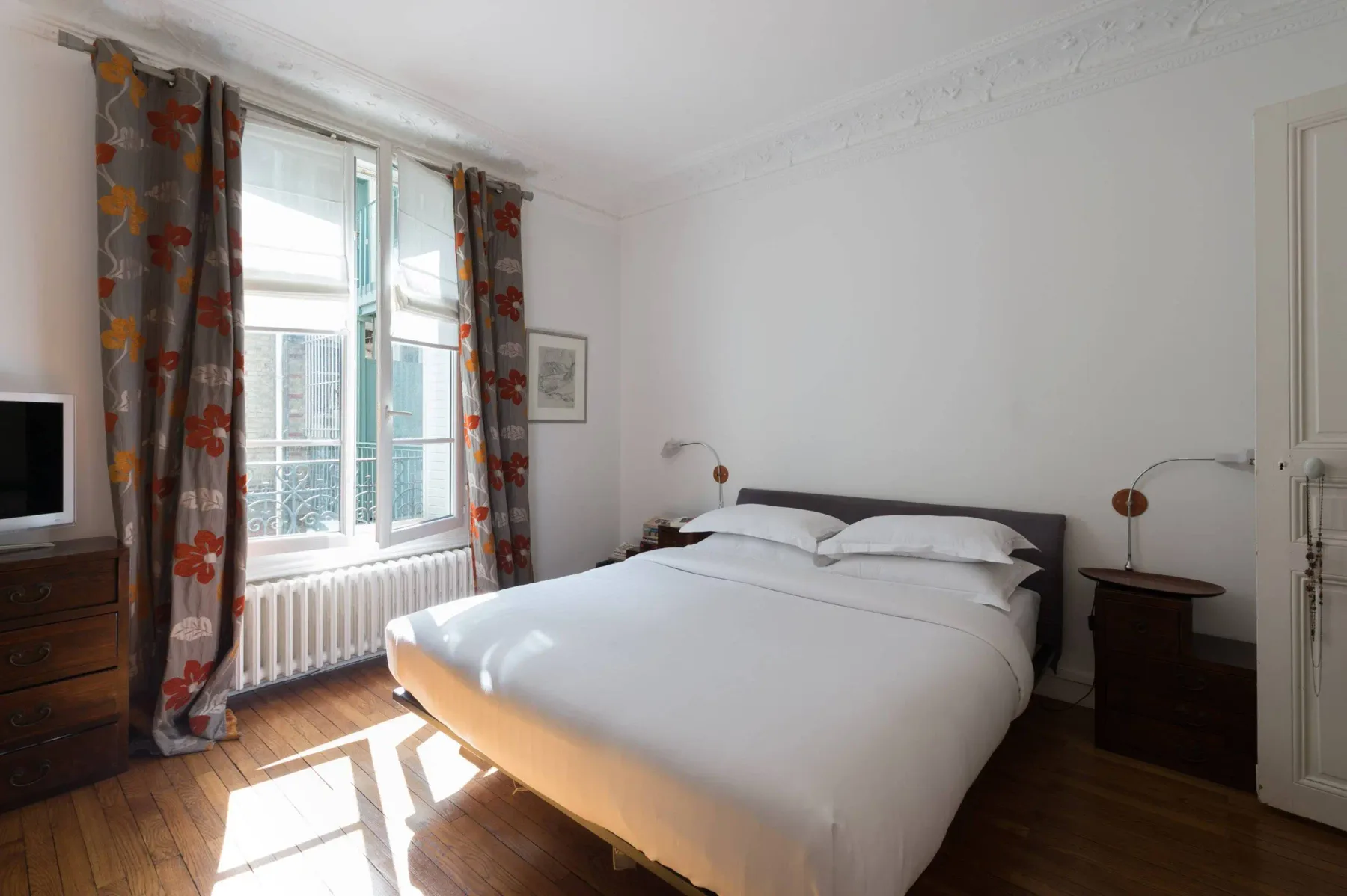Un dormitorio luminoso con una cama grande junto a ventanas altas y cortinas estampadas.