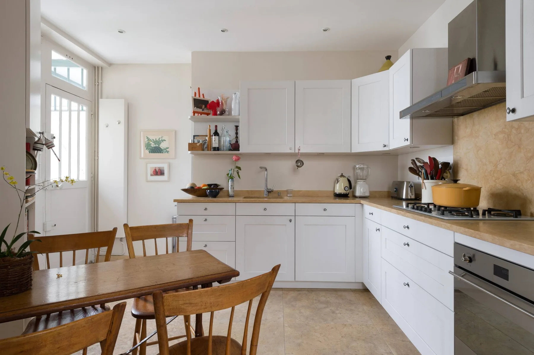 Una cocina luminosa con gabinetes blancos y una mesa de comedor de madera.
