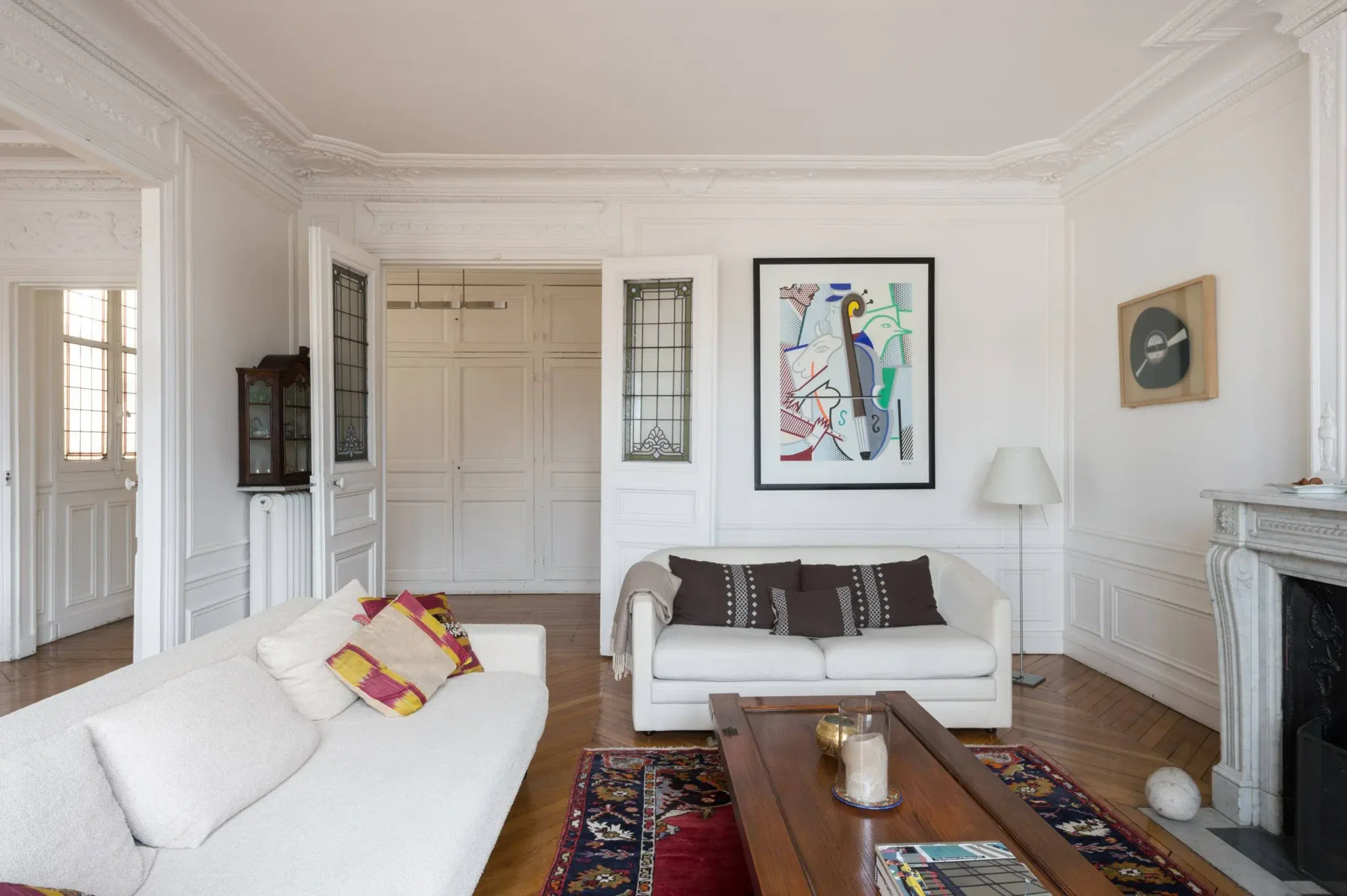 Una sala luminosa con asientos blancos, arte colorido y una mesa de centro de madera.