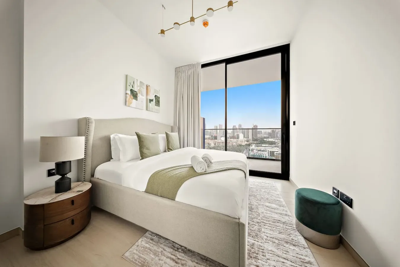 Un dormitorio luminoso con una cama tendida junto a un gran ventanal con vistas a la ciudad.
