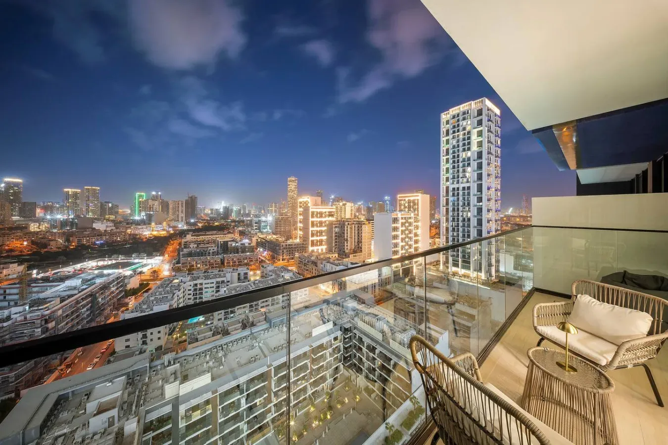 Un balcón con asientos ofrece vistas del horizonte urbano iluminado al anochecer.