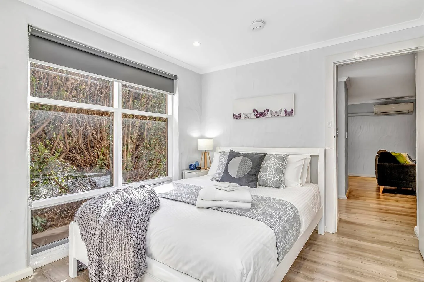 Un dormitorio luminoso tiene una cama tendida junto a una ventana grande.