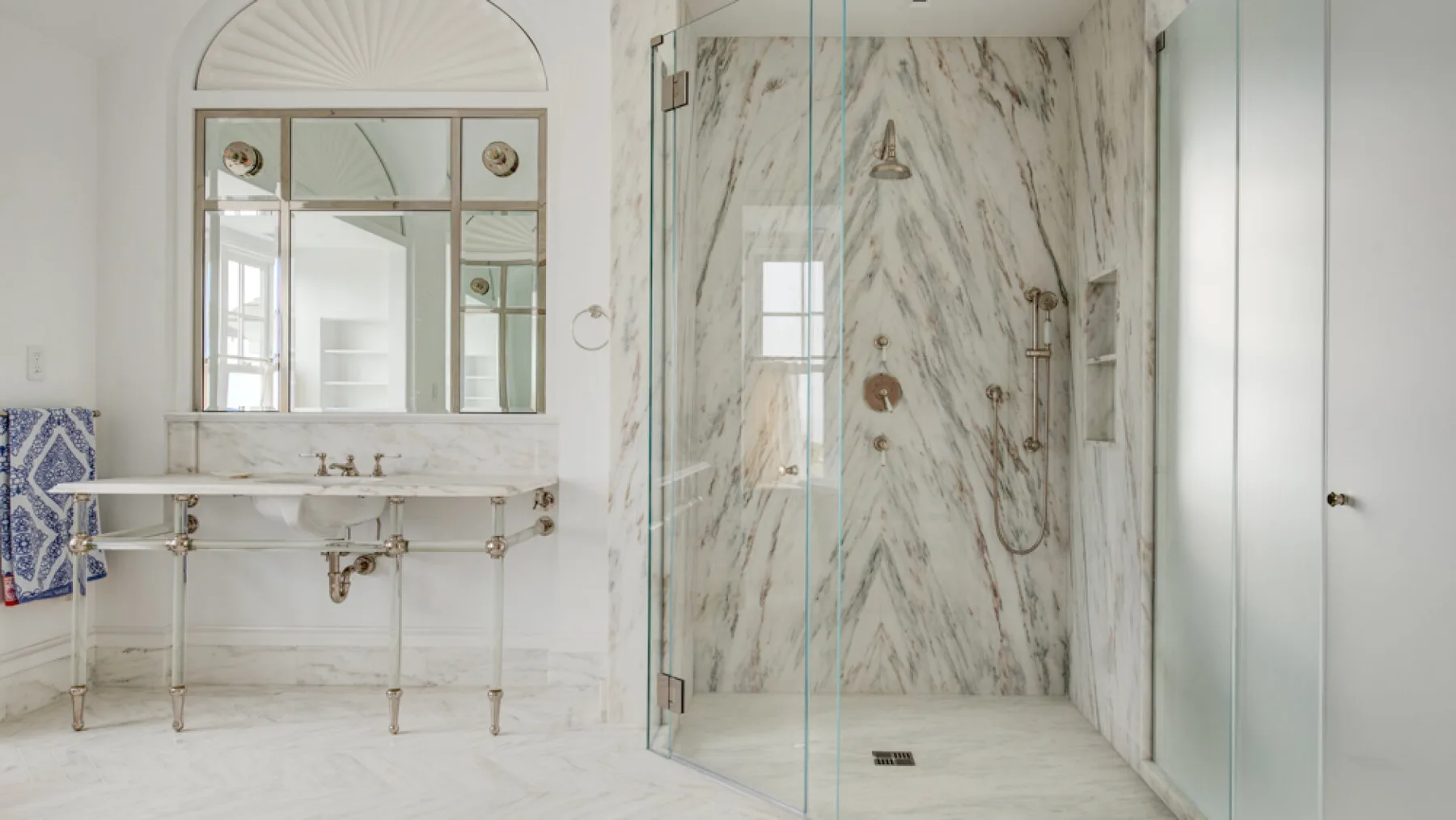 Un baño luminoso con una ducha de mármol y un lavabo con pedestal.