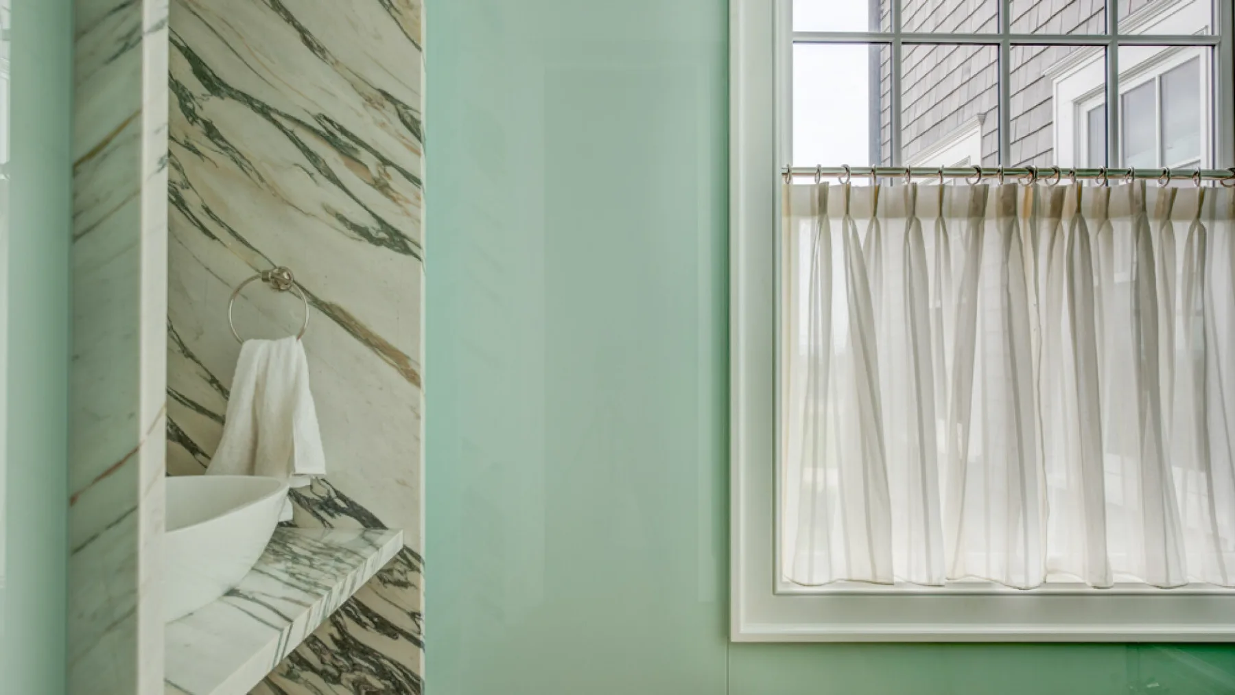 Un lavabo de baño con un fregadero sobre la encimera está junto a una gran ventana con cortinas.