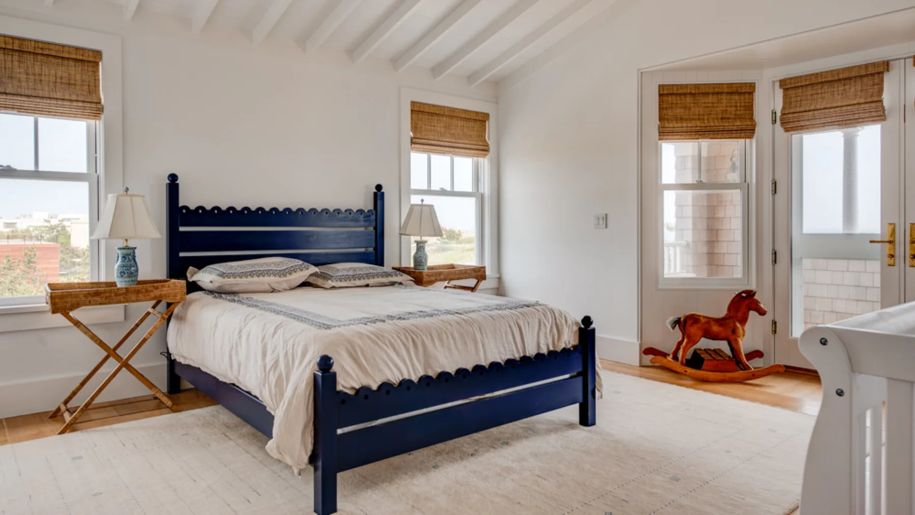 Un dormitorio luminoso con una cama azul marino y ventanas con persianas tejidas.