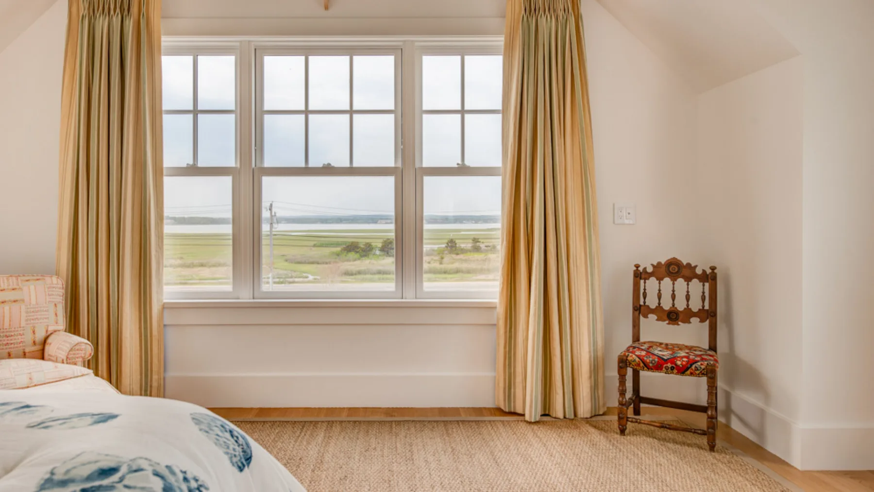 Un dormitorio luminoso con una ventana grande y una silla estampada.