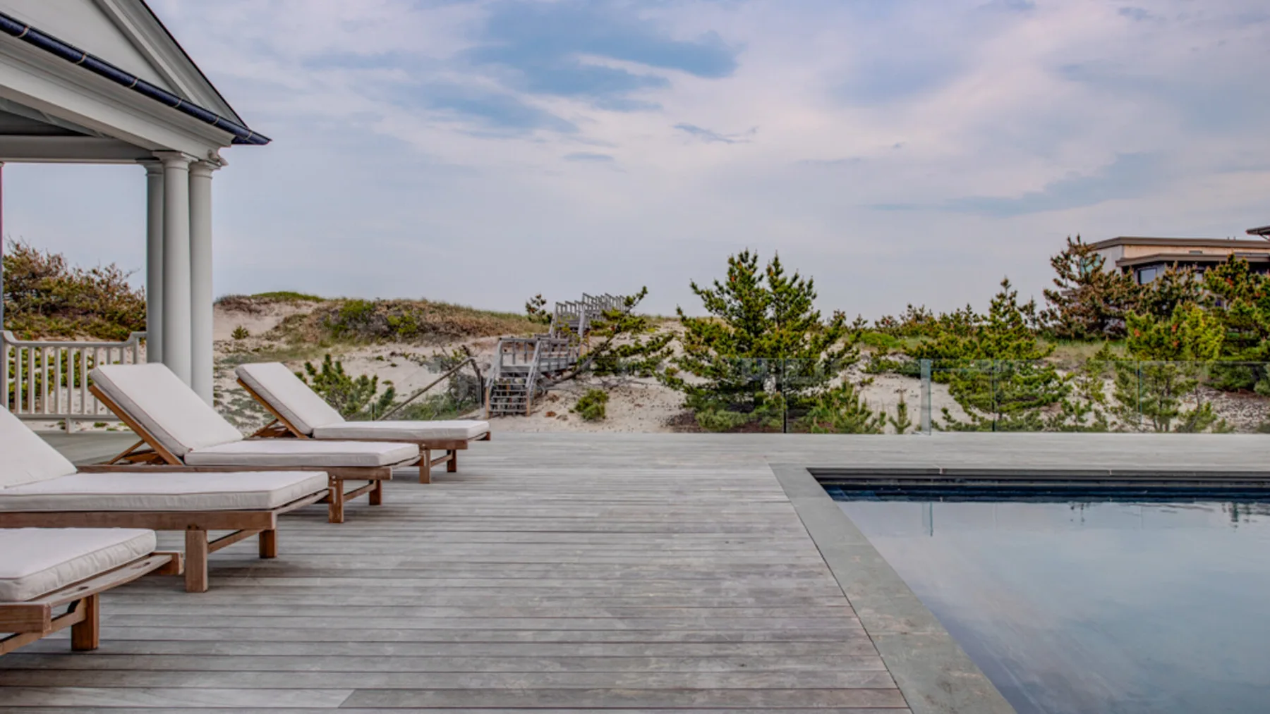 Una terraza exterior junto a una piscina, con asientos reclinables y vegetación costera.