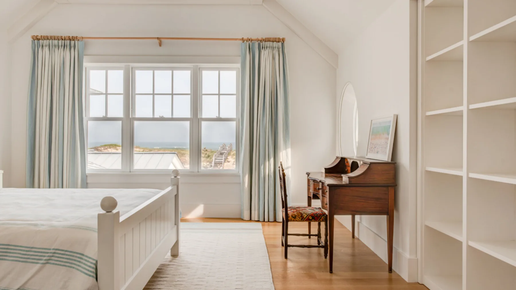 Un dormitorio luminoso con una cama, un escritorio y ventanas grandes.