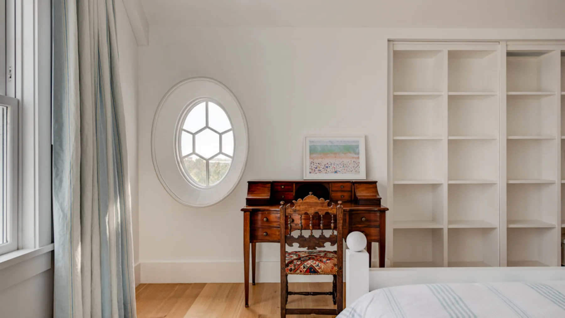 Un dormitorio luminoso con un escritorio de madera, estantes empotrados y una cama.