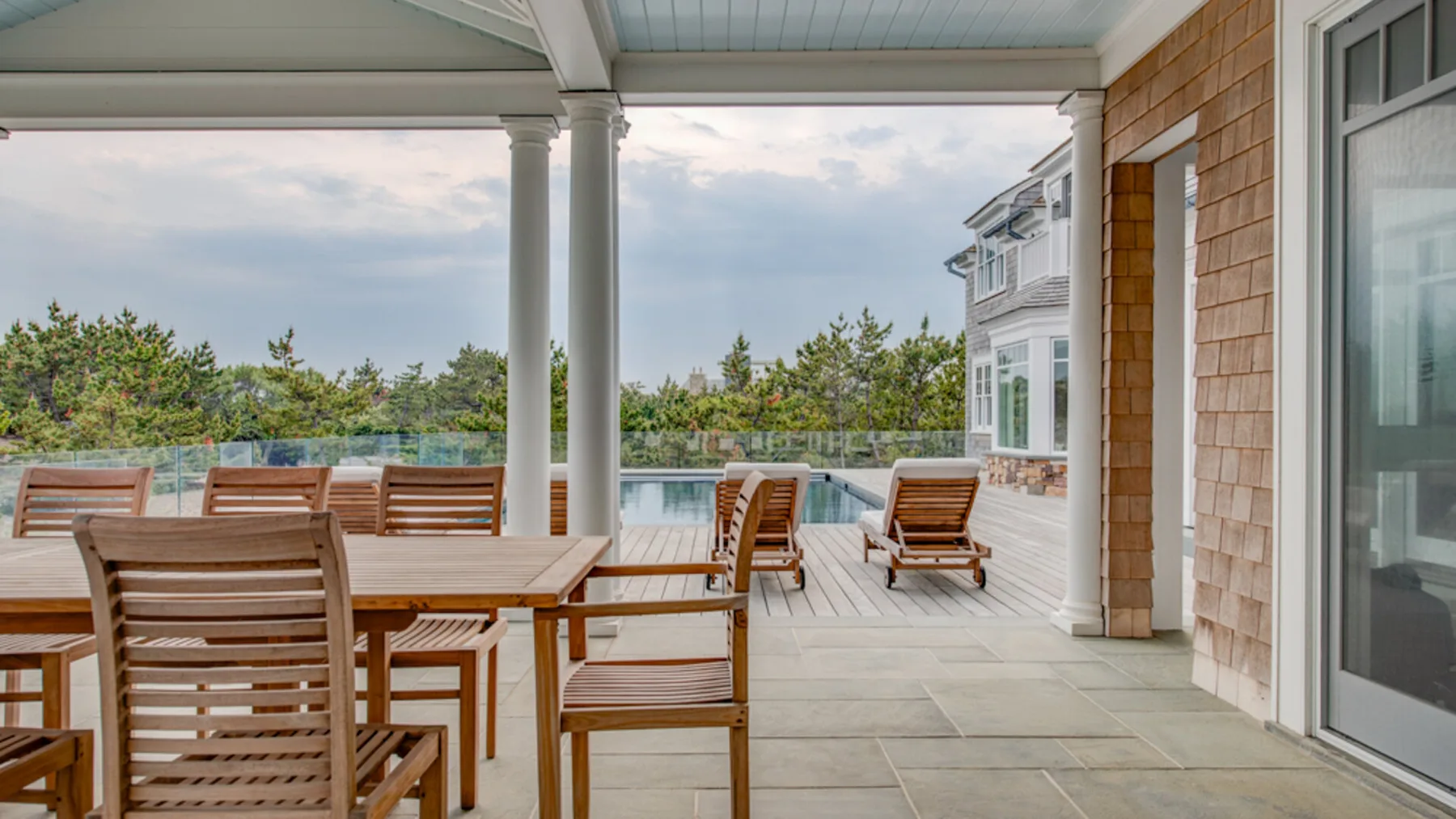 Un patio exterior cubierto con asientos de madera da a una piscina y vegetación.