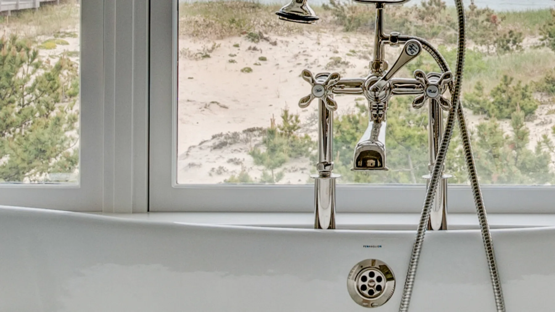 Un grifo de bañera y una ducha de mano están frente a una ventana.