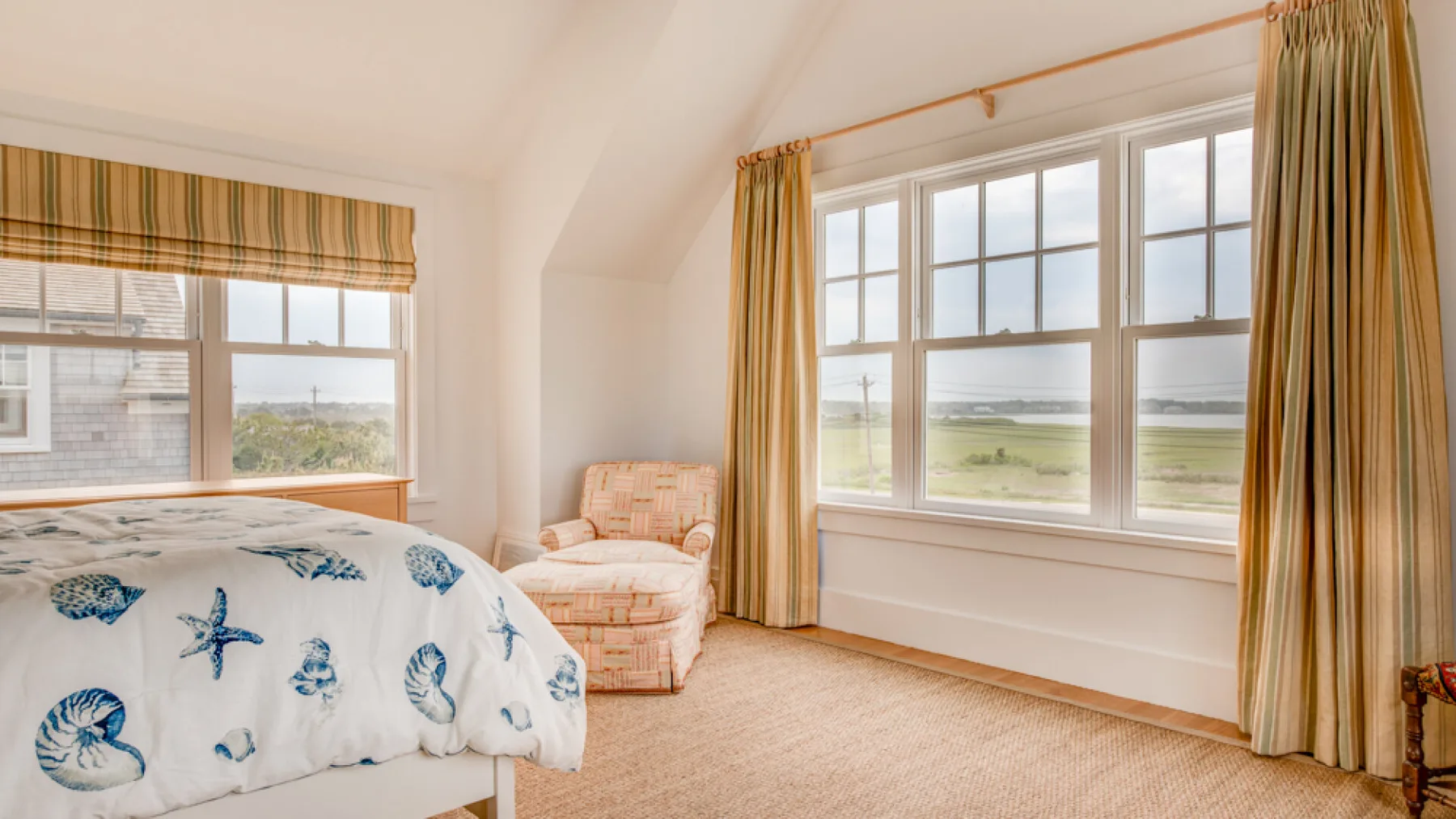 Un dormitorio luminoso con una colcha estampada y grandes ventanas con vistas a un paisaje verde.