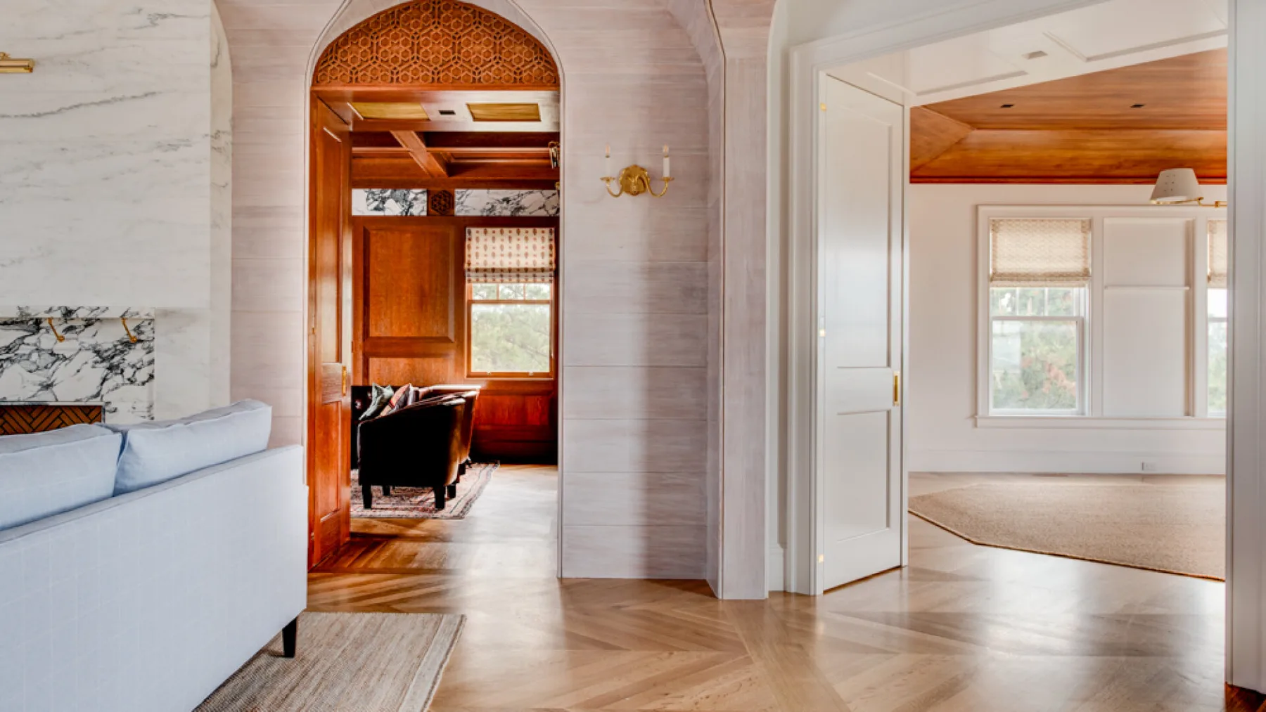 Un pasillo interior luminoso conecta una sala de estar con una habitación de techo revestido de madera.