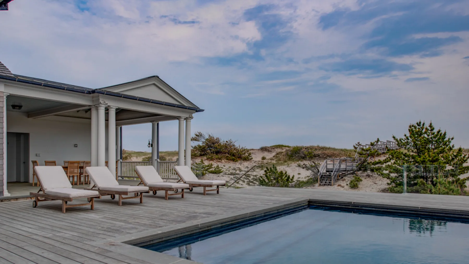 Una piscina junto a una terraza de madera da a dunas de arena y al mar.
