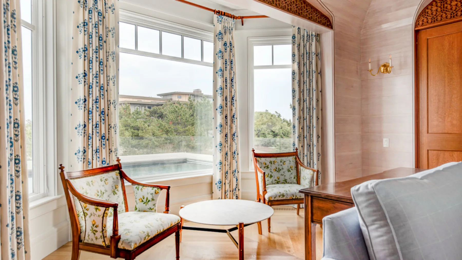 Una sala de estar luminosa con ventanas grandes, cortinas estampadas y asientos tapizados.