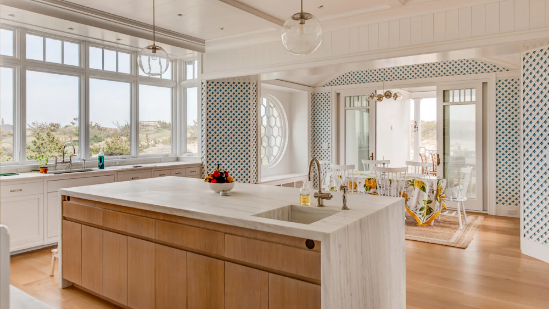 Una cocina luminosa con una isla grande y una mesa de comedor junto a ventanales.