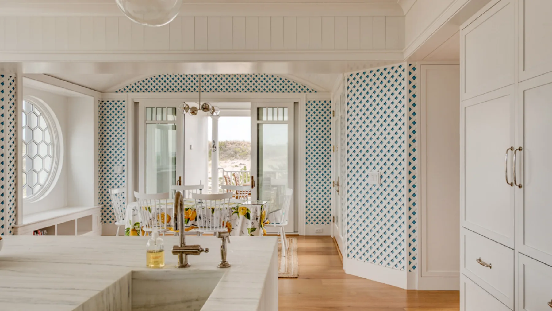 Una cocina luminosa con una isla de mármol y un comedor al fondo.