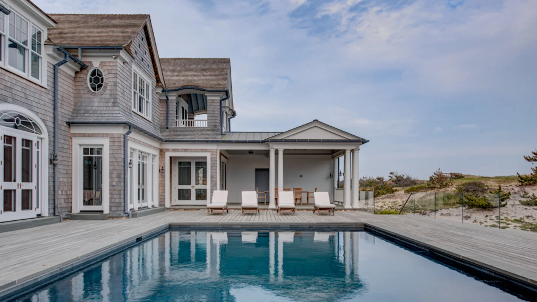 Una casa junto al mar da a una piscina y una amplia terraza de madera.