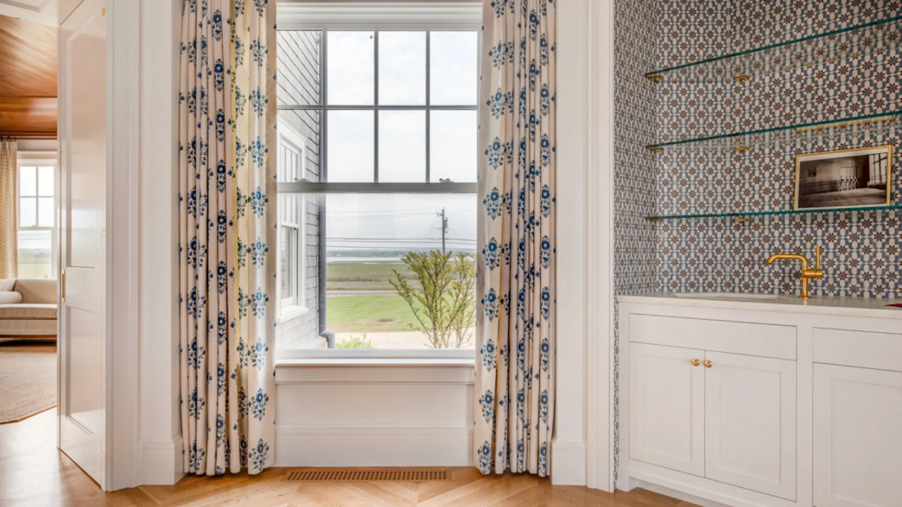 Una habitación luminosa con una ventana grande y cortinas estampadas junto a un tocador con azulejos.