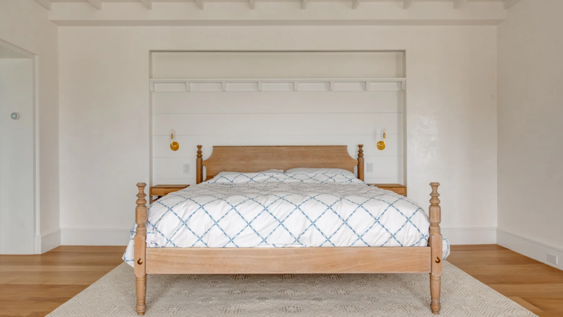 Un dormitorio con una cama de madera vestida con ropa de cama blanca y azul.