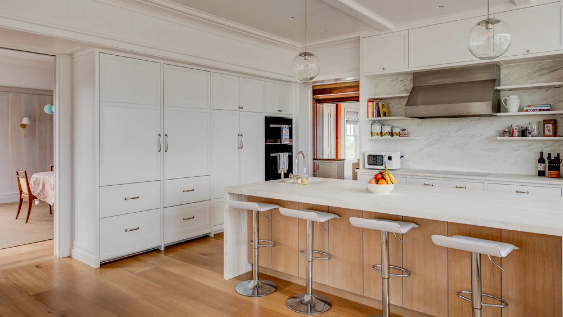 Una cocina luminosa con una isla larga, asientos de barra y gabinetes blancos.