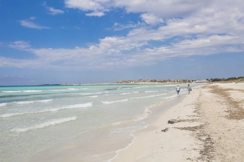 A sandy beach meets shallow waves beneath a partly cloudy sky.