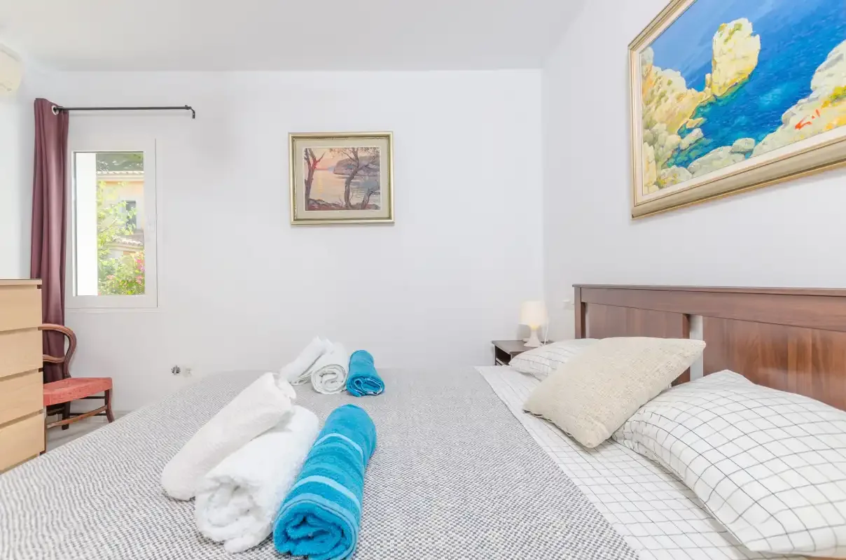 A bedroom with a bed, rolled towels, and framed wall art.