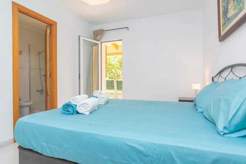A bedroom with a bed dressed in turquoise bedding and a doorway to a bathroom.