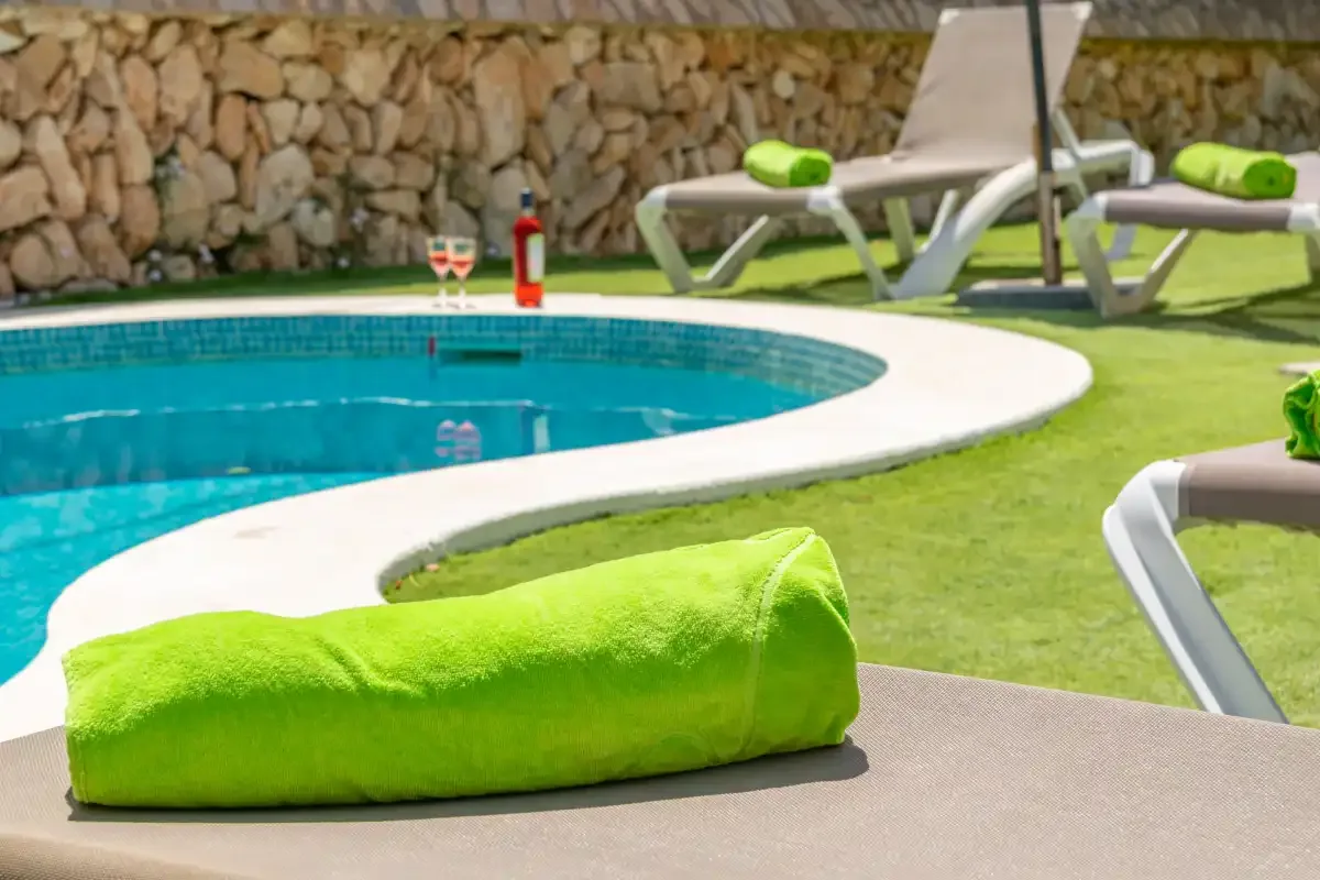 A swimming pool curves beside green lawn and loungers.