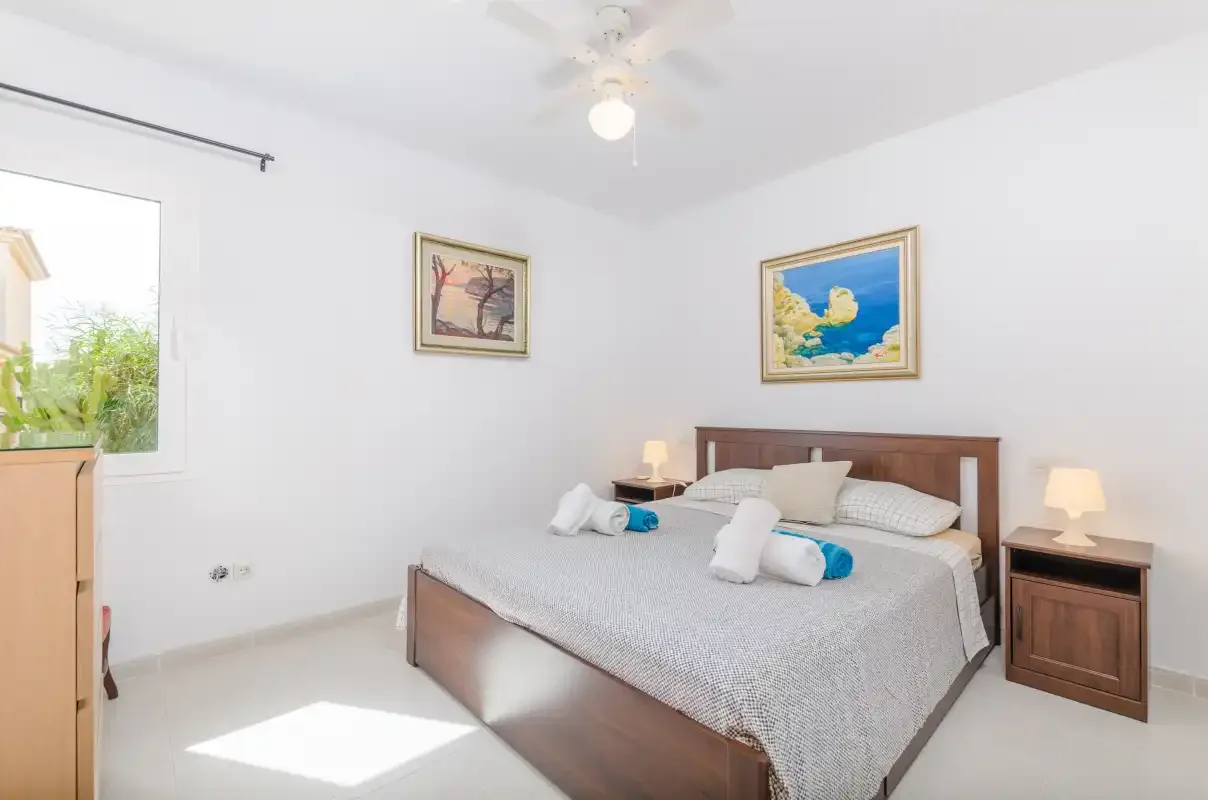 A bright bedroom has a double bed, framed pictures, and a window.