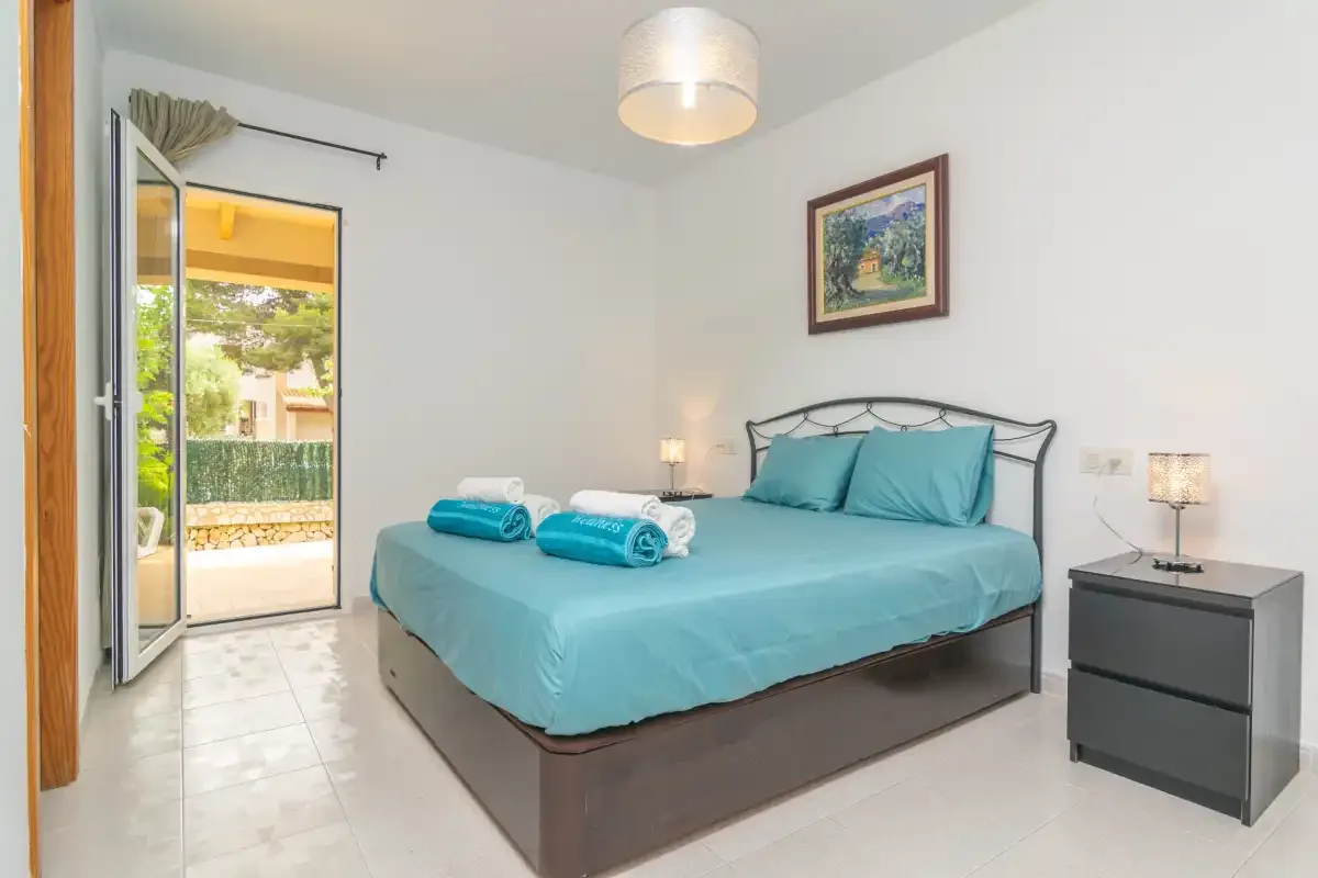 A bright bedroom with a bed dressed in turquoise bedding and an open balcony door.