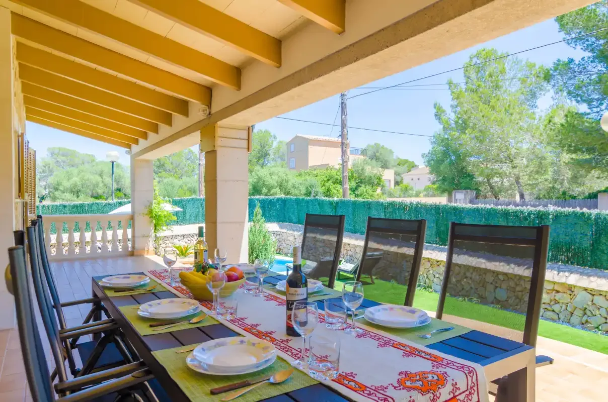 A covered outdoor dining area with a set table overlooking a garden.