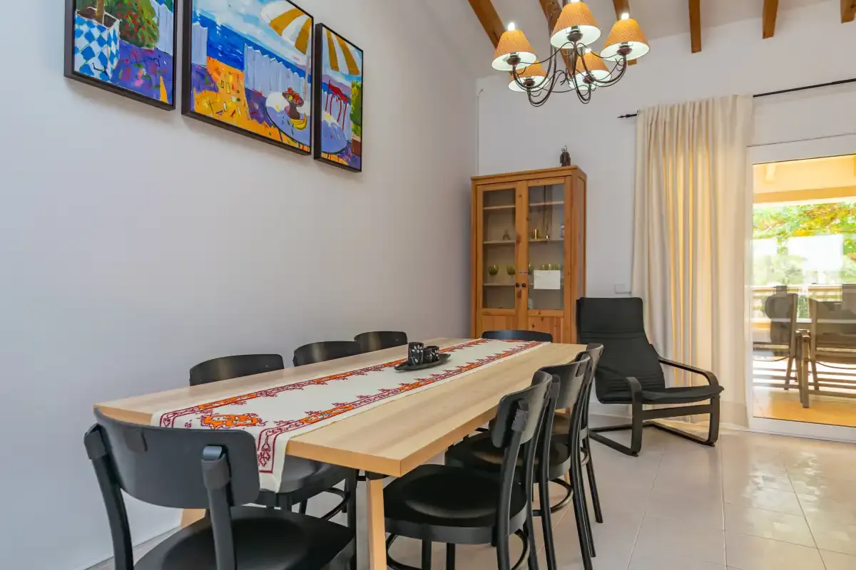 A dining area with a long table, dark seating, and colorful framed artwork.