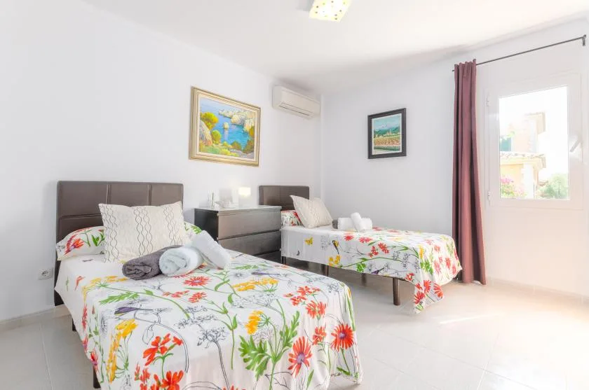A bright bedroom with two beds dressed in colorful floral bedding.