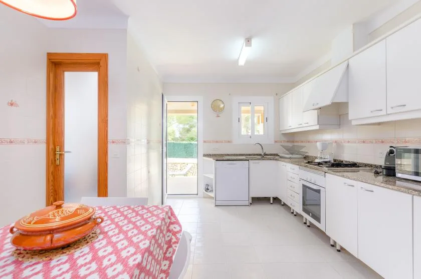 A bright kitchen with white cabinets, a countertop, and a patterned tablecloth in the foreground.