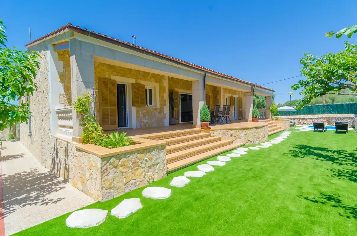 A stone house opens onto a covered patio beside a green lawn.