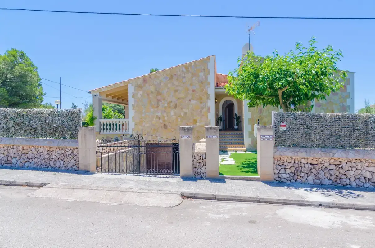 A stone-fronted house stands behind a low wall and metal gate.
