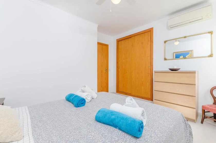 A bedroom with a bed, folded towels, and a dresser.